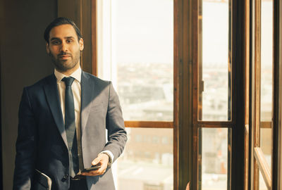 Portrait of confident male advisor standing by window at legal office