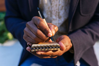 Cropped unrecognizable african american male entrepreneur sitting on bench in urban park and writing plans in notebook