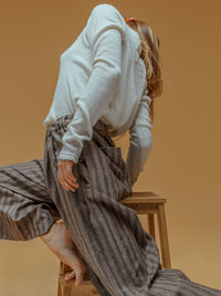 Low angle view of woman standing on stool against yellow background