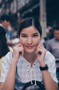 Close-up portrait of smiling young woman pulling cheeks while sitting outdoors
