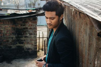 Young man standing by weathered house