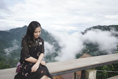 Woman sitting on railing against mountain