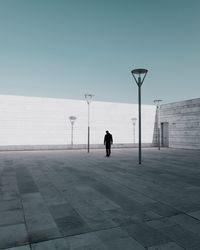 Rear view of man walking on footpath in city against clear sky