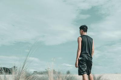 Rear view of man standing on beach against cloudy sky