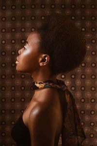 Side view of young woman standing by patterned wall