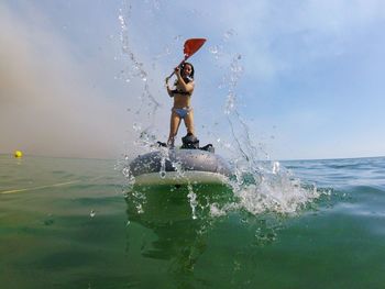 Cheerful young woman standing on inflatable raft in sea against sky