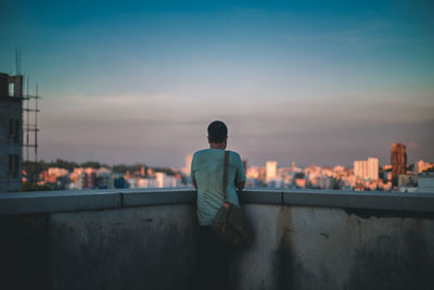 Rear view of man standing against cityscape during sunset