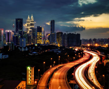 Light trails on road amidst buildings against sky at night