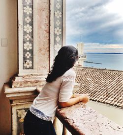 Side view of woman looking at sea while leaning on railing against sky