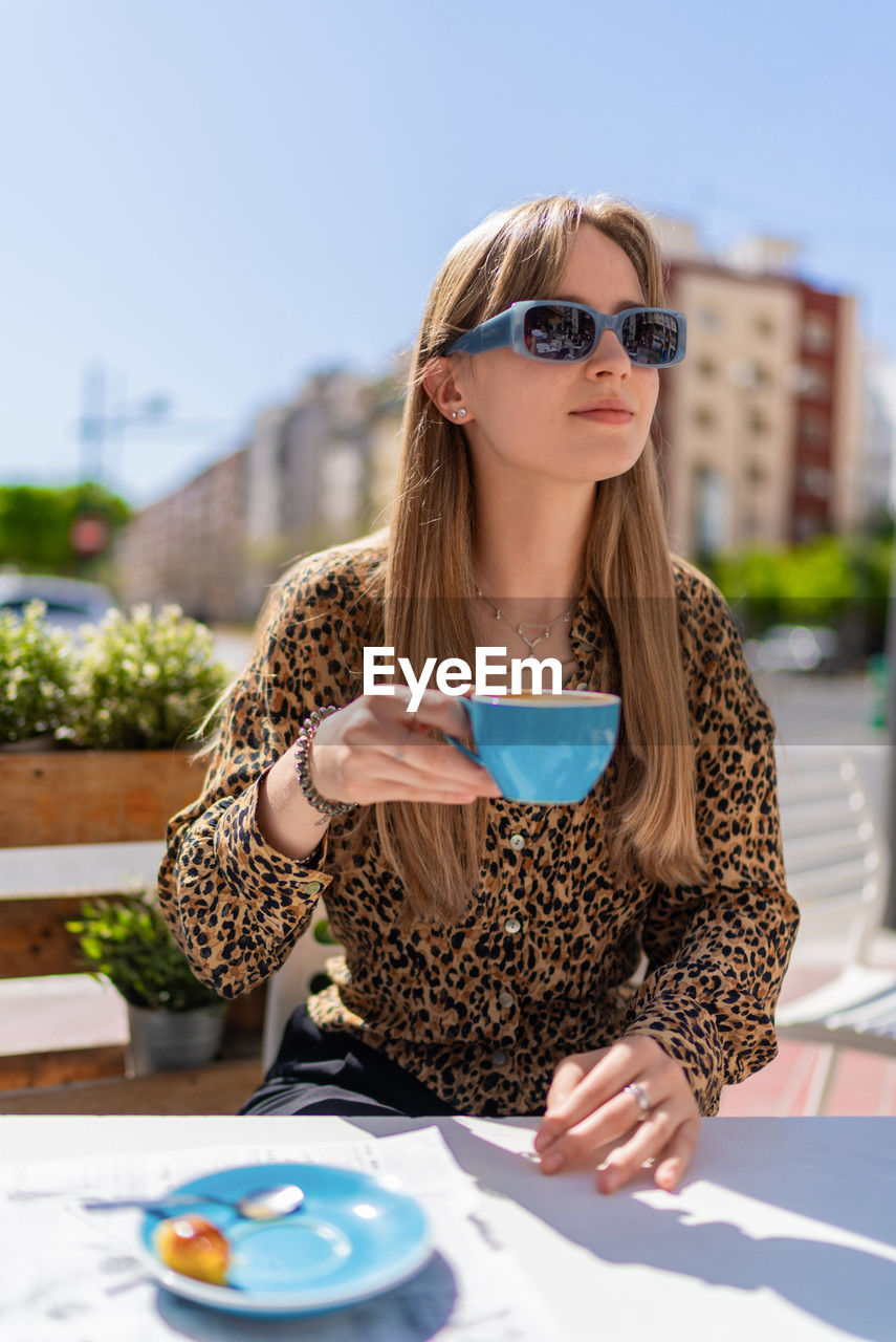 portrait of woman holding coffee while sitting on table in cafe