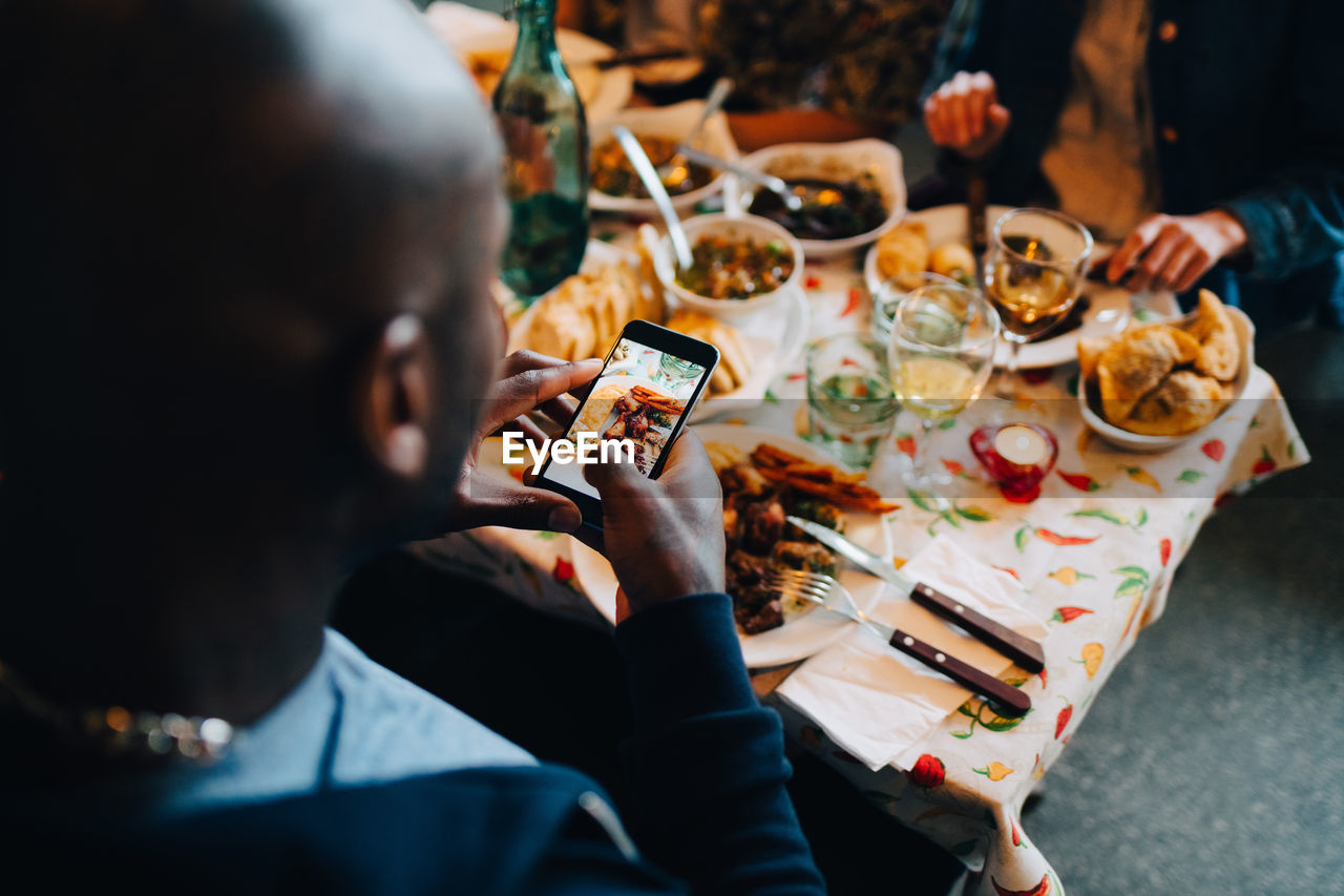 High angle view of young man photographing food in plate while sitting at restaurant during dinner party