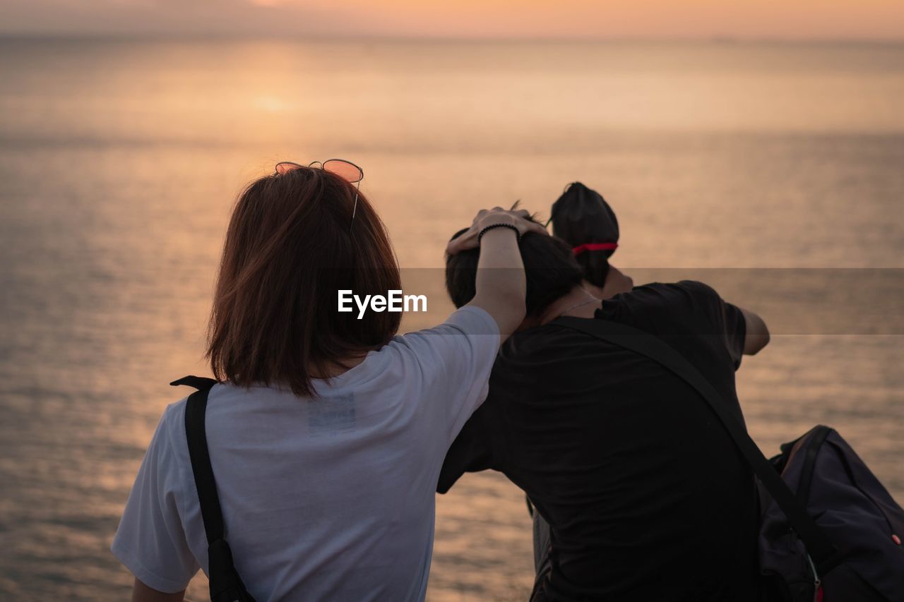 Rear view of couple sitting at beach during sunset