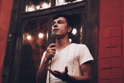 Young man holding microphone while standing against wall