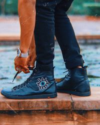 Low section of person tying shoelace while standing on retaining wall