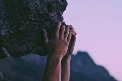 Close-up of hand holding rock against sky