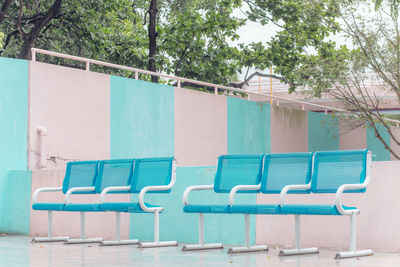 Empty chairs by swimming pool against trees and building