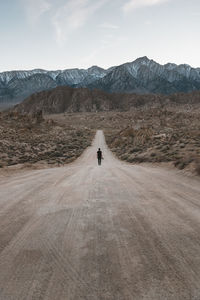 Rear view of man walking on dirt road against sky